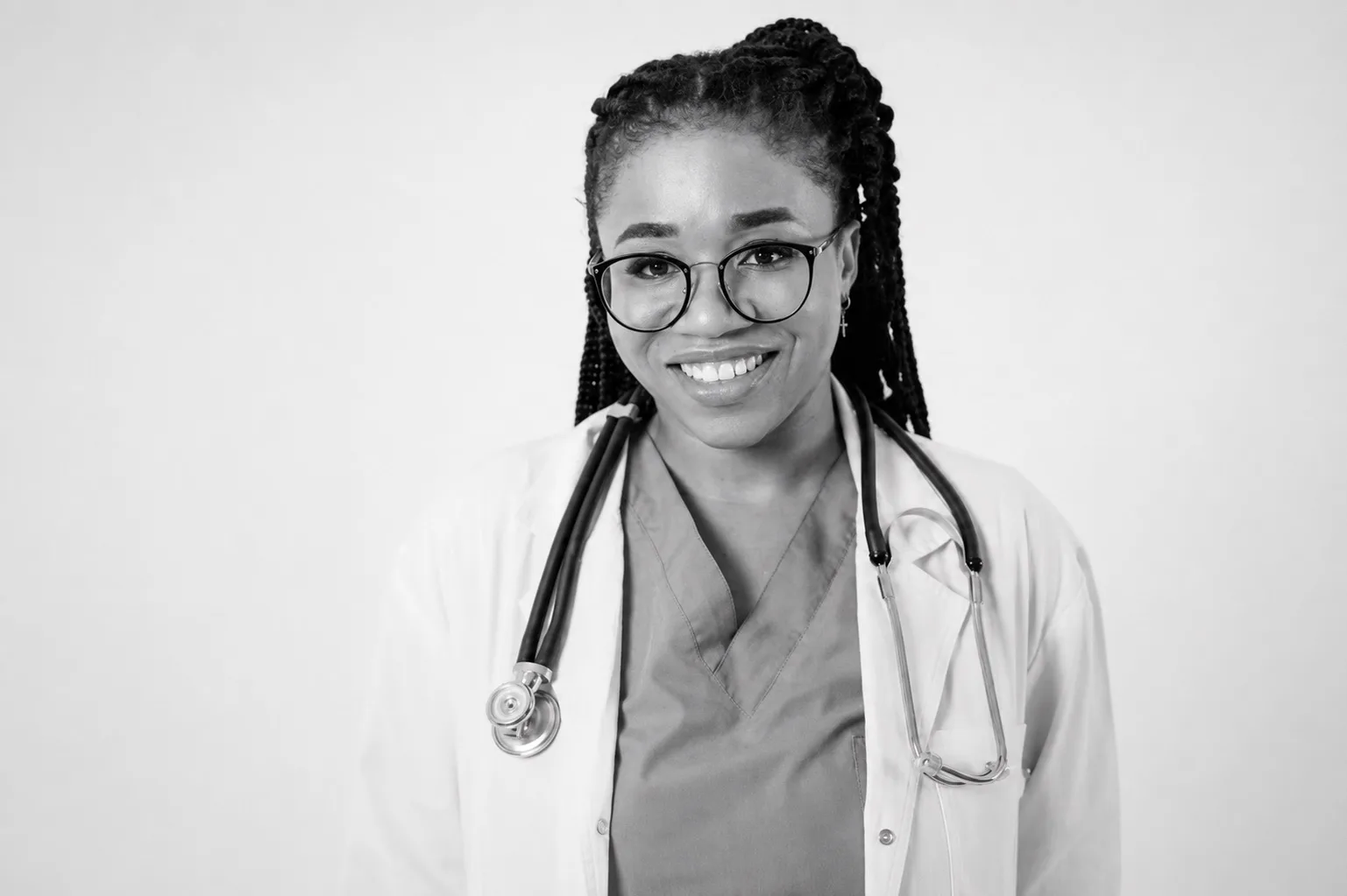 Black-and-white portrait of a smiling physician in glasses and a white coat, stethoscope around her neck, looking directly at the camera
