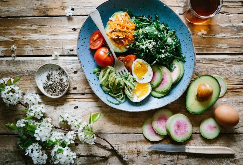 Overhead view of a healthy bowl meal with greens, tomatoes, a boiled egg and a halved avocado